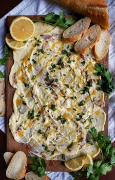 a wooden cutting board topped with cheese and bread next to sliced lemons on top of a table