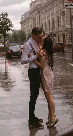 a man and woman kissing in the rain on a city street with cars behind them