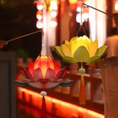 three colorful lights hanging from strings in front of a building with red and yellow flowers