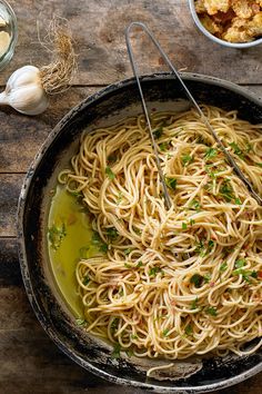 a pan filled with pasta and vegetables on top of a wooden table next to garlic