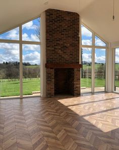 an empty living room with large windows and wood flooring in front of a brick fireplace