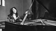 a black and white photo of a woman sitting in front of a grand piano smiling