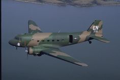 an airplane flying over the water in camouflage