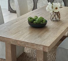 a bowl of green apples sitting on top of a wooden table next to a vase with flowers