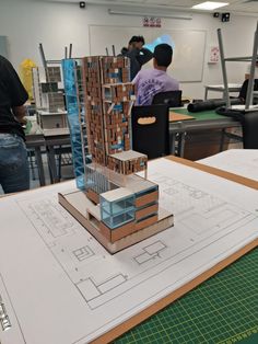 a model of a building on top of a table with people working in the background