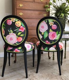 two black chairs with pink flowers painted on them in front of a dresser and mirror