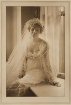 an old photo of a woman wearing a veil and sitting on a window sill