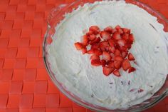 a bowl filled with white frosting and strawberries on top of an orange mat