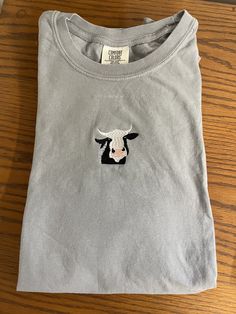 Embroidered Cow T Shirt Message me for sizes that are not listed!  Shirt:  Comfort Colors short sleeve grey t shirt 6.1 oz., 100% ringspun cotton Care Instructions:  Machine wash cold, hang to dry  Material on the back of the embroidery is designed to stabilize the shirt as it is being embroidered, it will soften over time with more washes. Visit my Etsy for more Nature-Inspired clothing : https://Stitchesbylindseyk.etsy.com Cute Cotton T-shirt With Cow Print, Cute T-shirt With Machine Embroidery And Short Sleeves, Casual Crew Neck Shirt With Machine Embroidery, Cute Gray Cotton T-shirt, Cute Short Sleeve Cow Print T-shirt, Casual Relaxed Fit T-shirt With Machine Embroidery, Cute Cow Print Cotton T-shirt, Casual Cotton Shirt With Machine Embroidery, Cute Cow Print Short Sleeve T-shirt