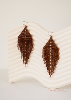 the brown beaded earrings are hanging off of a white stand on a striped wall