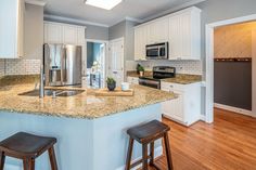 a kitchen with white cabinets and granite counter tops, two stools in front of the island