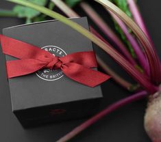 a black box with a red ribbon on it next to some vegetables and a plant