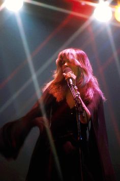 a woman singing into a microphone while standing in front of spotlights on a stage