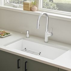 a white kitchen sink sitting under a window next to a plate of food on a counter