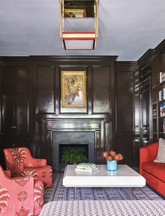 a living room with two red chairs and a white coffee table in front of a fireplace