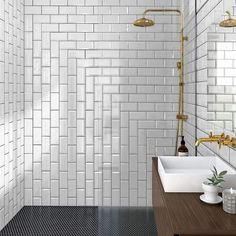 a white tiled bathroom with two sinks and gold faucets