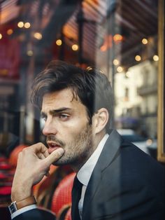 a man in a tuxedo is looking out the window with his finger to his mouth