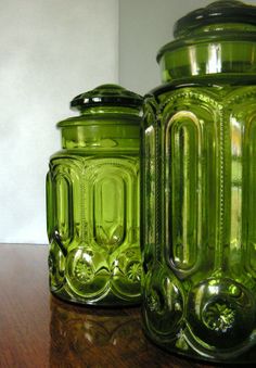 two green glass jars sitting on top of a wooden table next to eachother