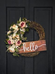 a wreath with the word hello painted on it is hanging on a black front door