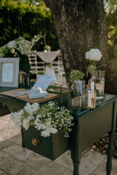 a green table with flowers and pictures on it in front of a tree at an outdoor wedding