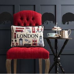 a red chair sitting next to a table with a cup and tea pot on it