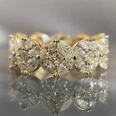 a yellow gold ring with three pear shaped diamonds on the front and center, sitting on a reflective surface