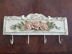 a white wall mounted shelf with pink roses on the top and two hooks attached to it