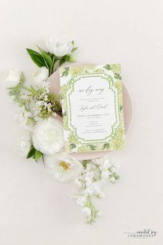 the wedding stationery is surrounded by white flowers and greenery, including peonies