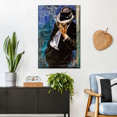 a living room with a blue chair and a painting on the wall next to a potted plant