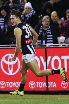 a male afl player is running on the field with his mouth open and people in the stands behind him