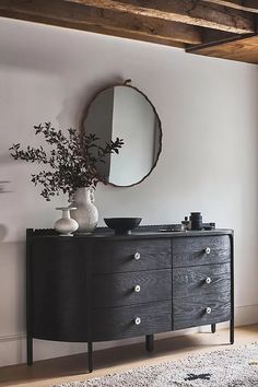 a black dresser with two vases and a round mirror on the wall above it