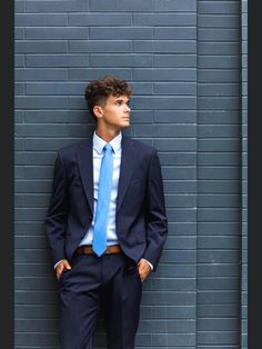 a young man in a suit and tie leaning against a wall with his hands on his hips