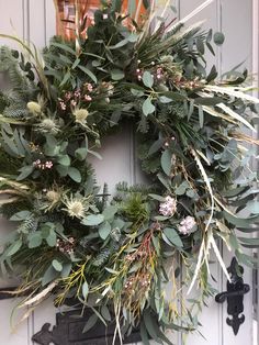 a wreath is hung on the front door with greenery and other foliage around it