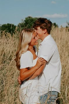 a man and woman are standing in the tall grass with their arms around each other