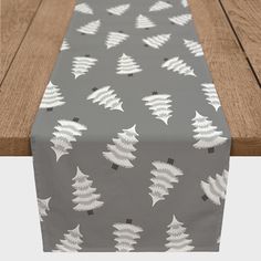 a table runner with white trees on grey and gray background, sitting on a wooden surface