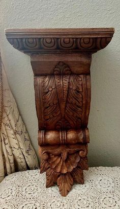 an ornate wooden vase on a lace covered tablecloth next to a curtain and pillow