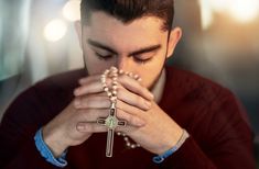 a young man wearing a red shirt is holding a rosary