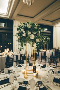 a tall centerpiece with white flowers and greenery sits on top of a round table