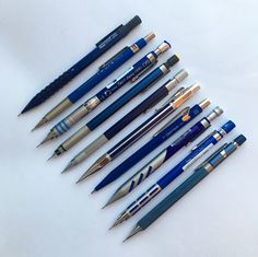 several pens lined up in a triangle on a white surface with one pen pointed at the other