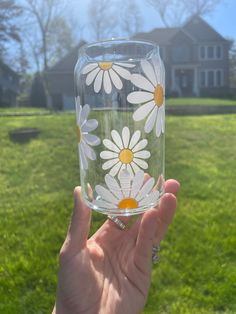 a hand holding up a glass with daisies painted on the outside and inside, in front of a house