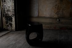 a black vase sitting on top of a wooden floor next to a wall with peeling paint