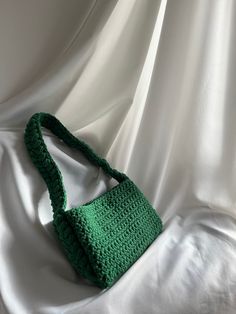 a green crocheted purse sitting on top of a white sheet