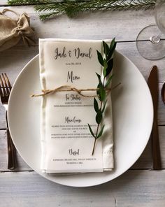 a place setting with napkins, silverware and greenery on a white plate