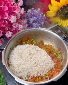 a pot filled with rice and vegetables on top of a stove next to colorful flowers