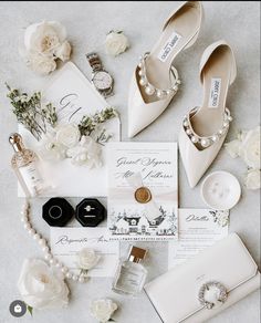 the wedding stationery is laid out with white flowers and pearls on it's shoes