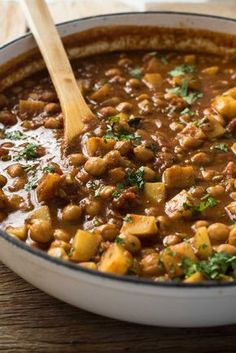 a large pot filled with stew on top of a wooden table next to a spoon