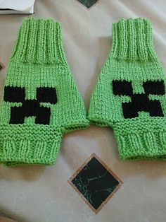 two green knitted mittens with black skulls on them sitting on top of a bed