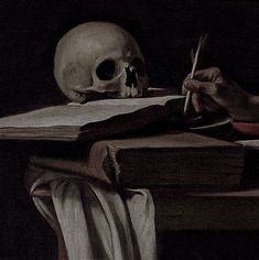 a skull sitting on top of a table next to an open book and a pen