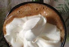 a cup filled with whipped cream sitting on top of a green table cloth next to a bottle