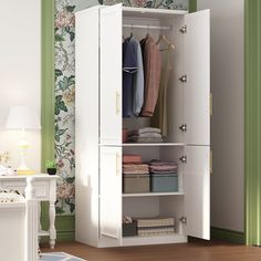 a white wardrobe with clothes hanging on the door and drawers in front of green wallpapered walls